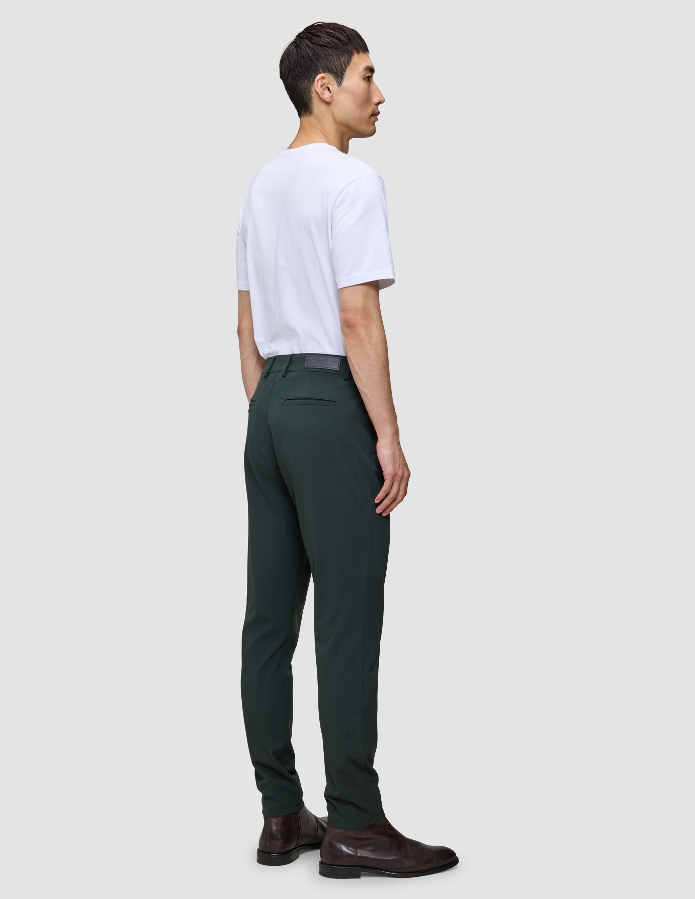 Eine Person, von hinten gesehen, die ein weißes T-Shirt und eine Ease Pants Slim Northern Pine sowie braune Lederstiefel trägt und damit das minimalistische skandinavische Design verkörpert.